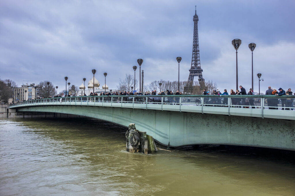 Parisians and tourists watch the great flood in Paris from bridge Pont de Alma. Zouave statue near Alma bridge shows water level in river Seine