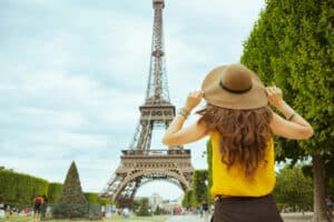 Seen from behind stylish solo tourist woman in yellow blouse and hat in Paris, France sightseeing.