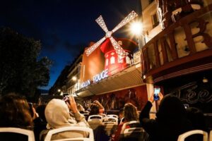 People in an upper deck bus night tour looking at Moulin Rouge