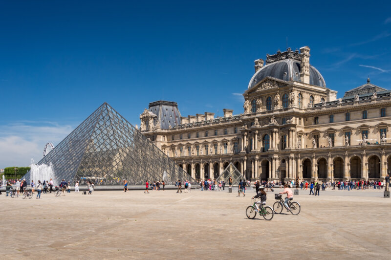 visitors and bikers around the louvre pyramid in paris france