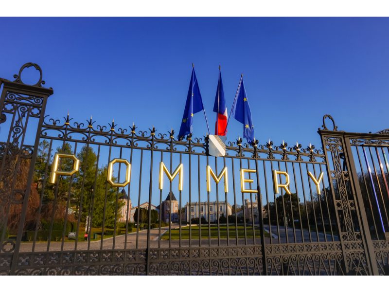 Gilded letters reading "Pommery", and flags, on the cast-iron gate