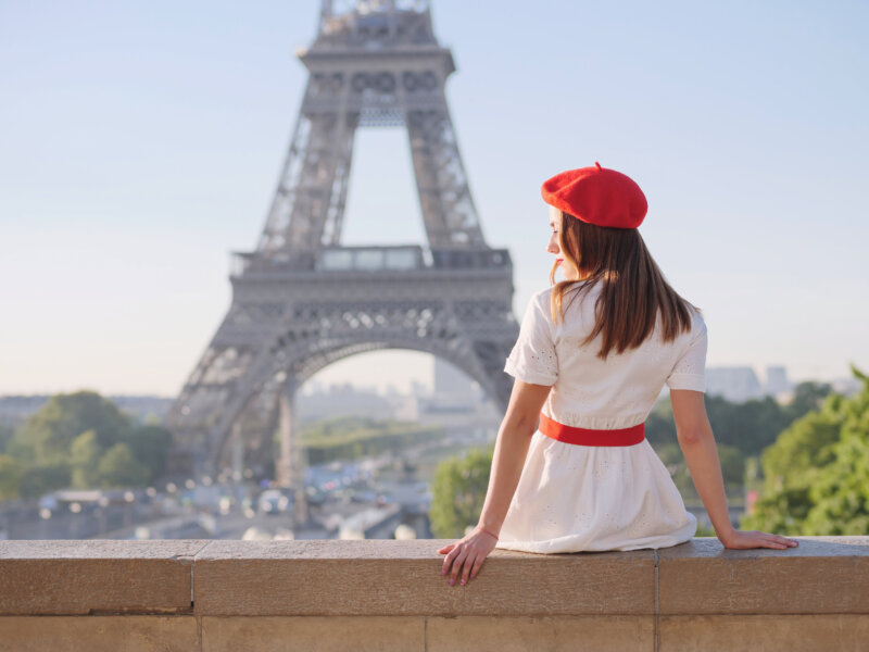 A beautiful girl in a white dress, a red beret sits against the backdrop of the Eiffel Tower in Paris 