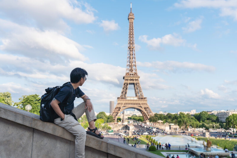 Man with backpack looking at Eiffel tower, famous landmark and travel destination in Paris, France. Traveling in Europe in summer