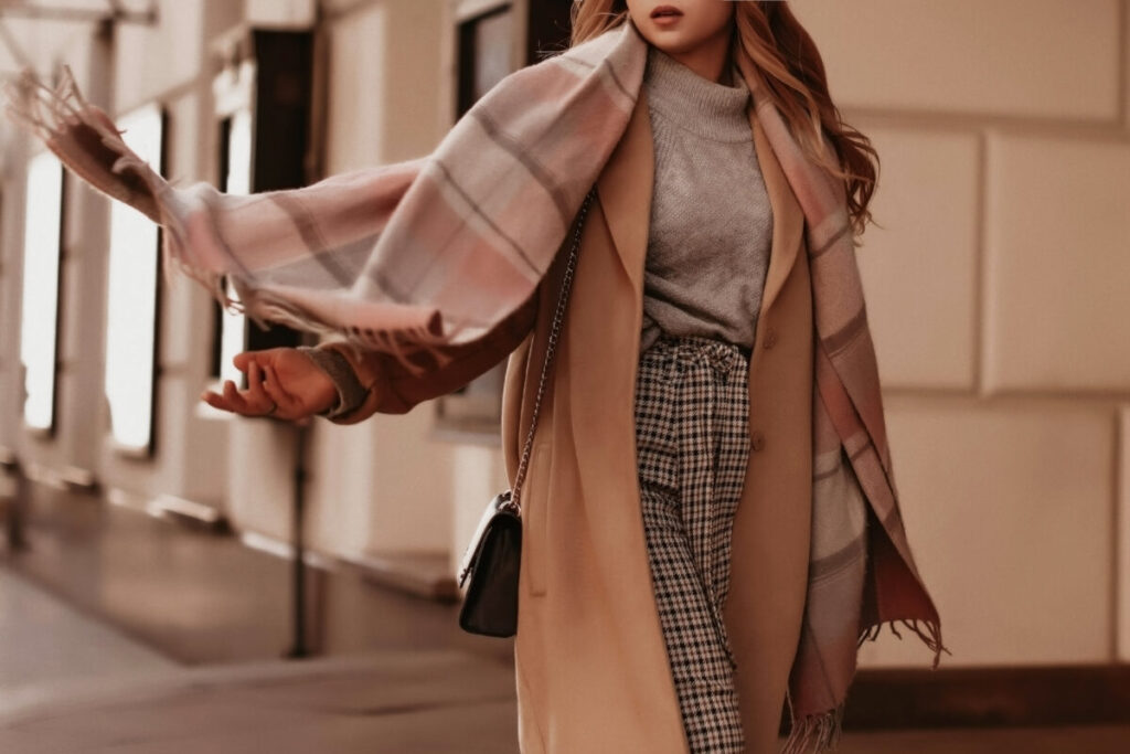 Young woman with cropped head in the grey knitted cozy sweater and brown coat walking on the street.