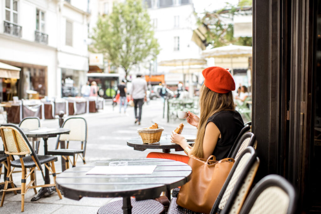 European sidewalk café scene with stylish woman, historic backdrop, daytime setting.