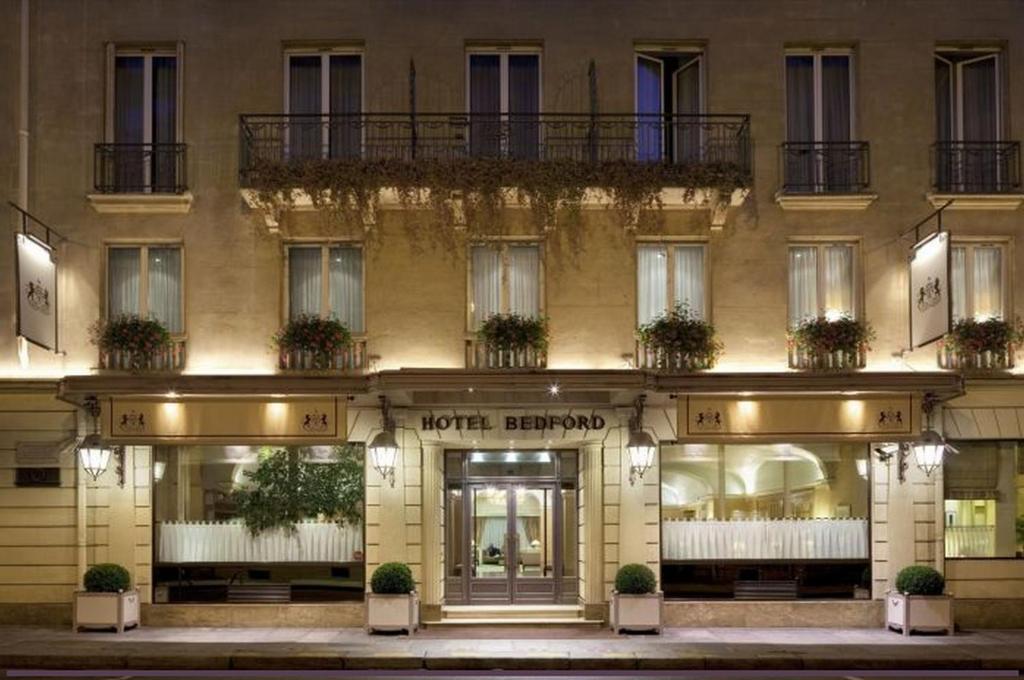 The façade of Hôtel Bedford Paris, an elegant 19th-century building adorned with intricate wrought iron balconies, welcomes guests with its timeless charm.