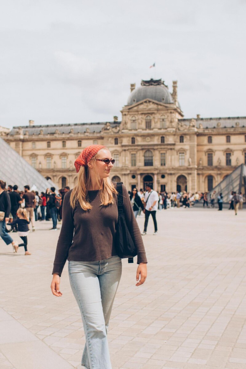 Woman in casual fashion near Louvre Museum, Paris, representing travel lifestyle in France.