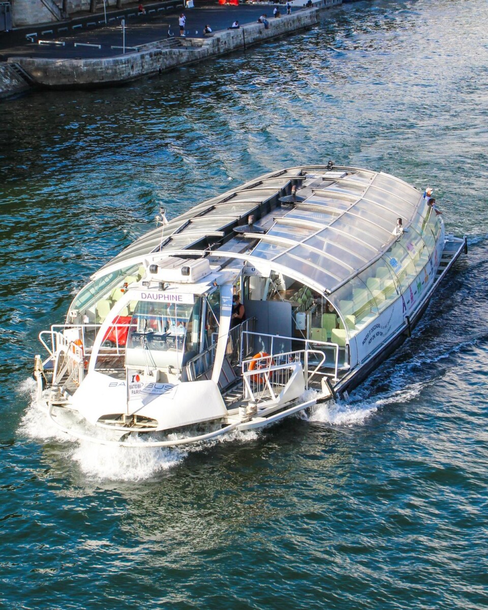 Discover Paris from the Seine river on a scenic cruise, glass-top boat passing iconic landmarks under blue skies.