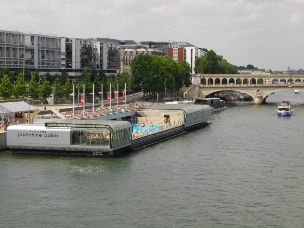 Outdoor swimming pool, Piscine Joséphine Baker, located on the Seine River in Paris, surrounded by city views.