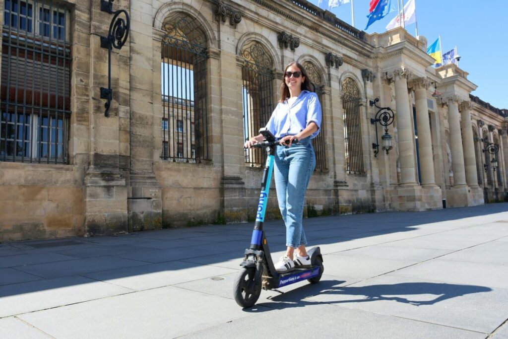 Woman rides an electric scooter near a stone building