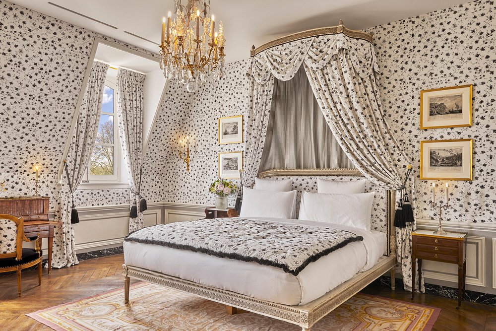 Elegant bedroom in Airelles Château de Versailles with a bed, a chair, and a stunning chandelier overhead.