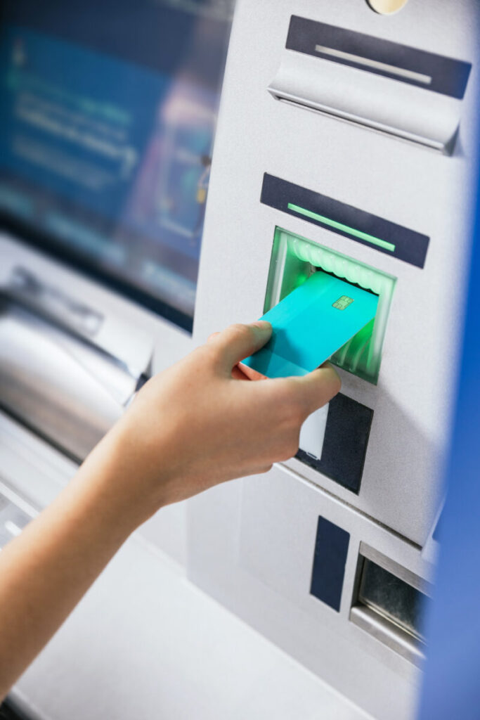 Close-up of a young woman’s hand using a credit card at an ATM to complete a money transfer or withdrawal.