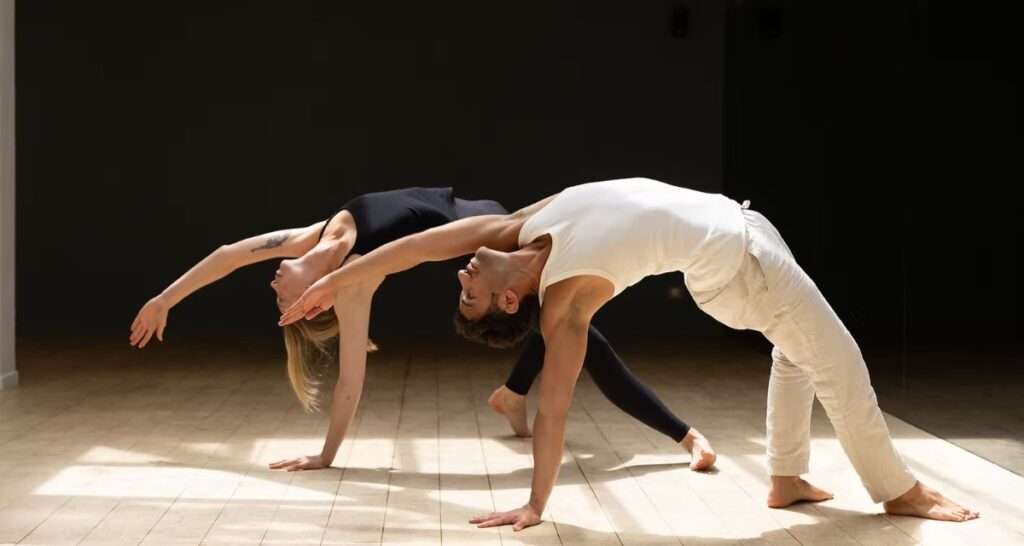 Two individuals perform a synchronized backbend pose in Bandha Yoga Studio Yoga Paris 6 , wearing contrasting black and white attire, conveying balance and grace.