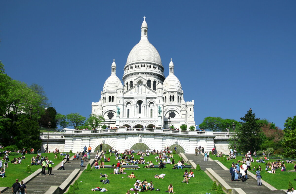 The Basilica of the Sacré-Cœur in Montmartre, a stunning white domed church overlooking Paris, surrounded by lush greenery.