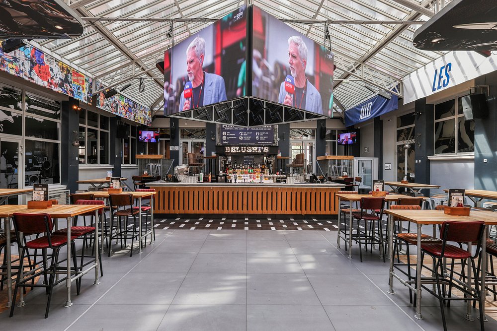 Interior of Belushi's restaurant in Paris, featuring tables and chairs arranged in front of a large screen.
