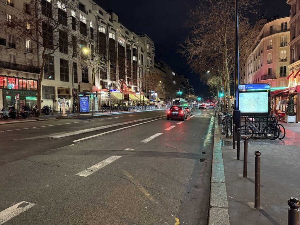 Nighttime scene on Boulevard Montparnasse, Paris, showcasing cars and people amidst vibrant city lights.