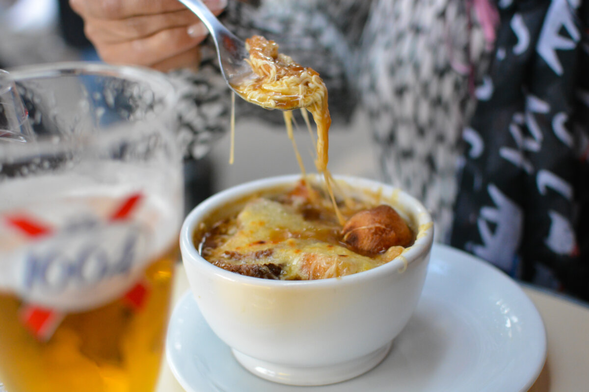 Steaming bowl of French onion soup and a cold beer are served at an outdoor cafe in Paris, capturing a delightful moment.