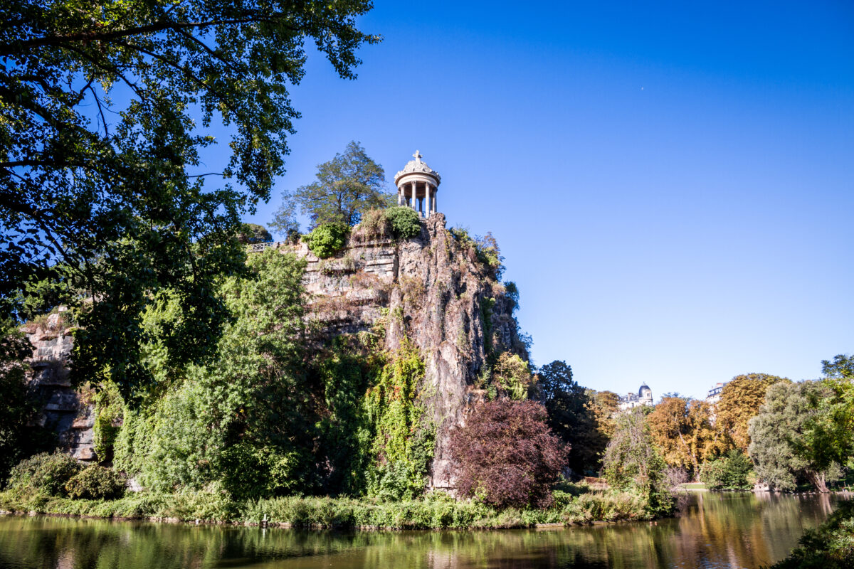 Sibyl temple overlooking a serene lake in Buttes-Chaumont Park, surrounded by lush greenery in Paris.