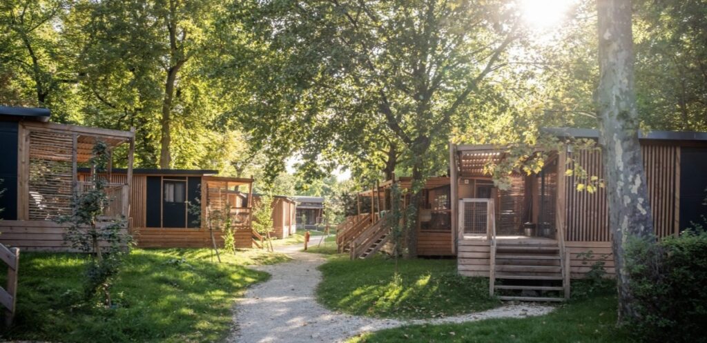Several rustic cabins nestled in a wooded area, surrounded by trees and grass at Camping de Paris.