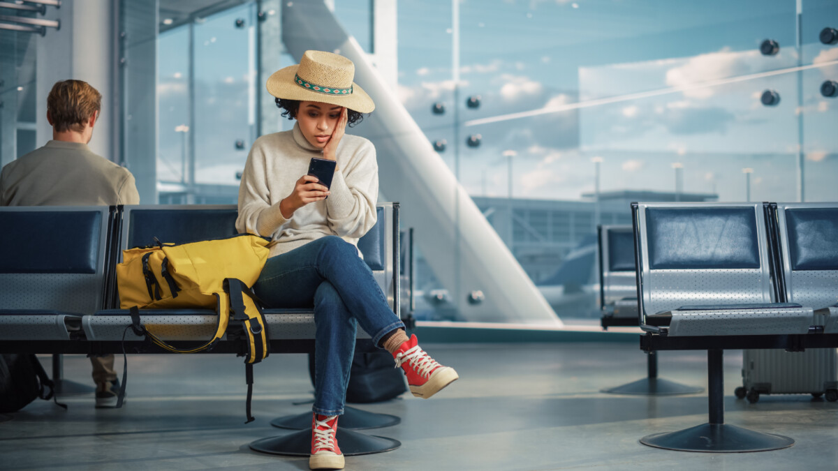 A Woman Waits for Flight, Uses Smartphone, Receives Shockingly Bad News, Misses Flight. Upset, Sad, and Dissappointed Person Sitting in a Boarding Lounge of Airline Hub.