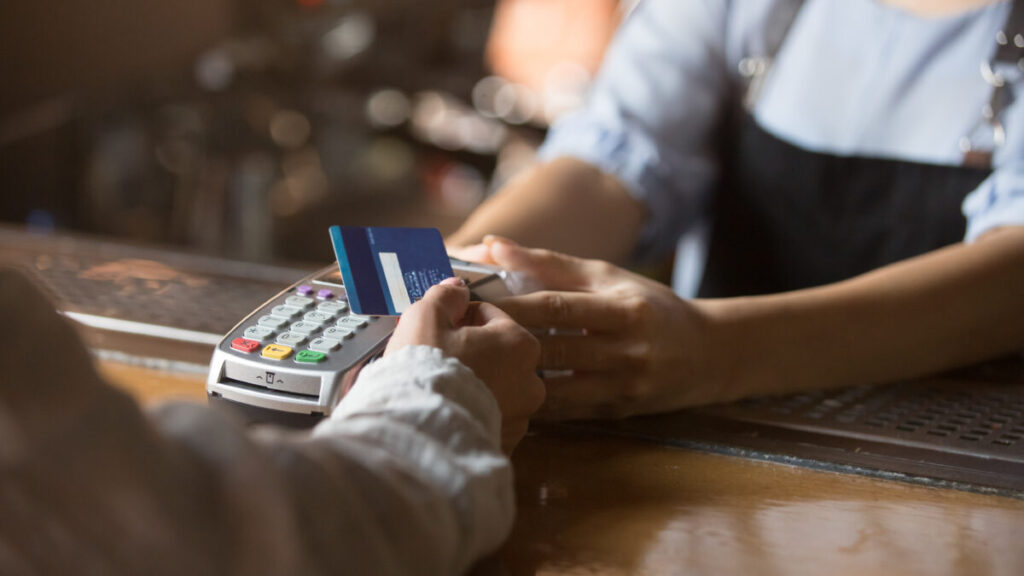 Woman using a credit card to make a contactless payment at a counter with NFC technology.