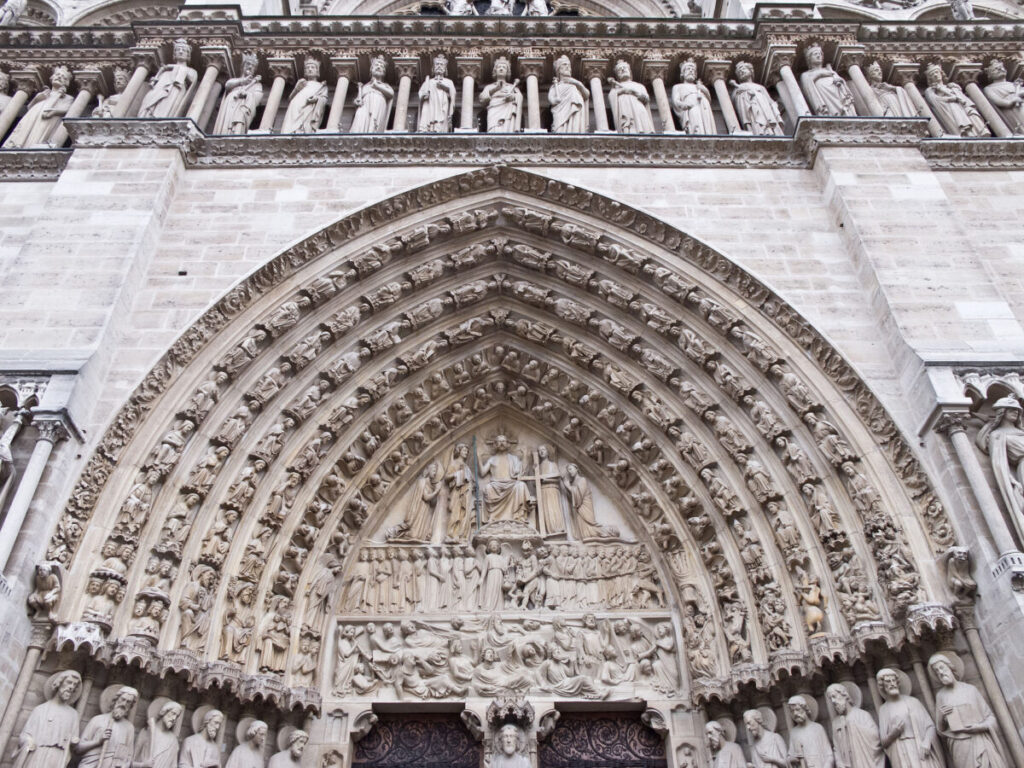Cathédrale Notre-Dame de Paris facade with intricate stone carvings of religious figures, arching rows of statues, and detailed reliefs, evoking a sense of grandeur and history.