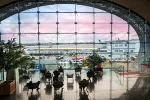 Tourists seated in the departure lounge gaze out at the airfield through a large oval window at Charles de Gaulle Airport.