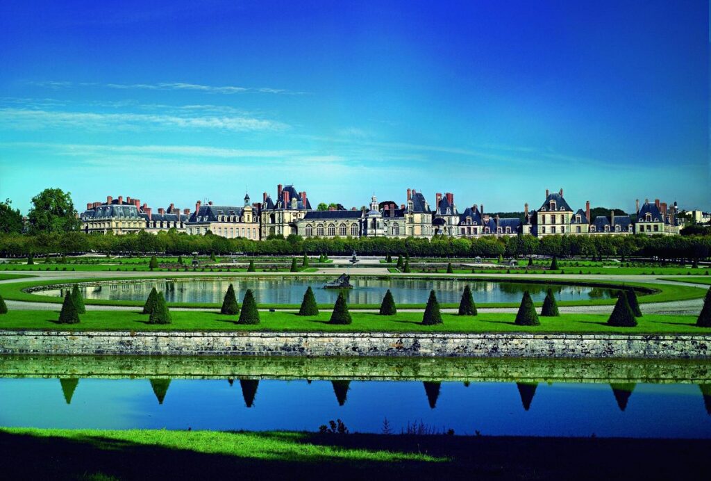 The stunning Château de Fontainebleau, France, with a large building and a peaceful pond situated in front of it.