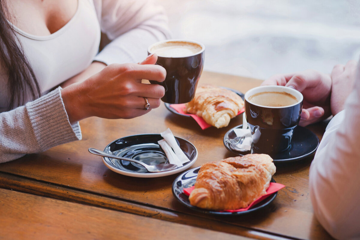 Close-up of a couple's hands sharing coffee and croissants at a cafe table, creating an intimate dining experience.