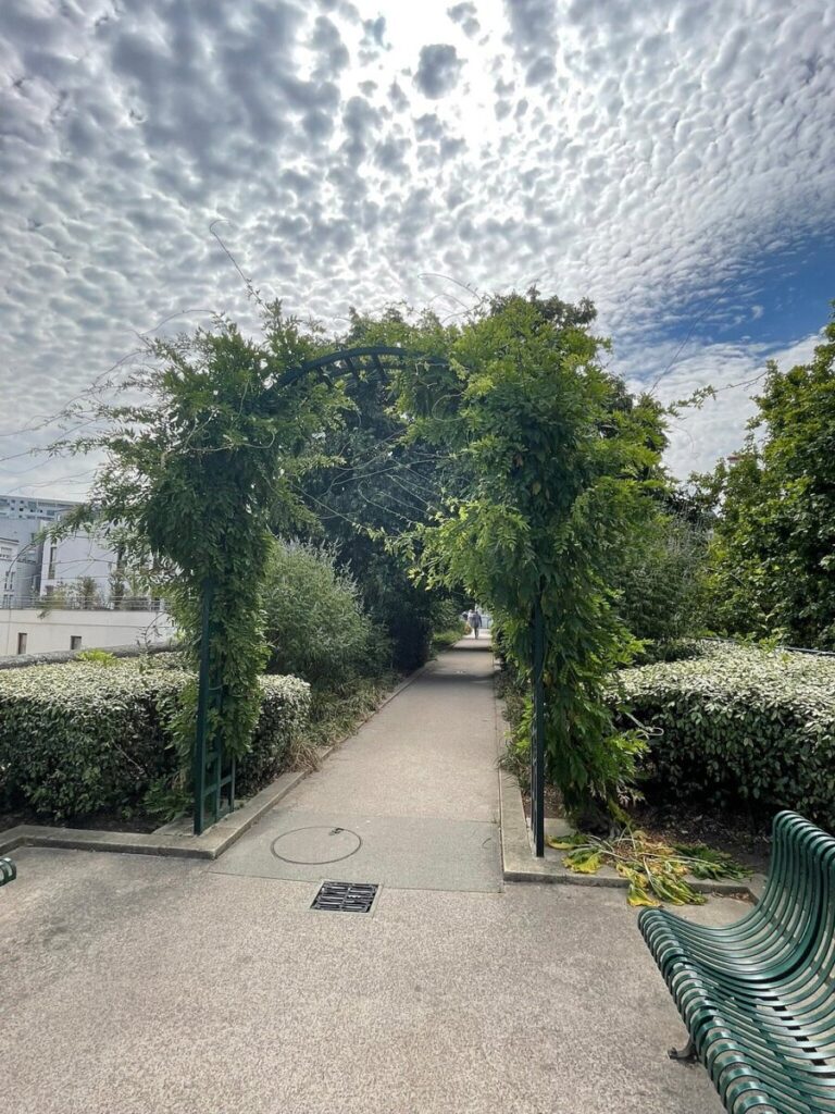 Solitary bench in a park with a blue sky backdrop, located at Coulée Verte René-Dumont, Paris, France.