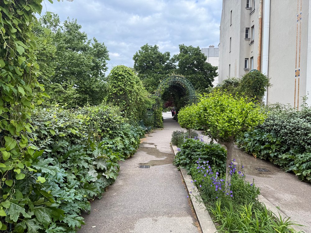 Vibrant pathway surrounded by plants and trees, leading to a building at Coulée Verte René-Dumont in Paris, France.