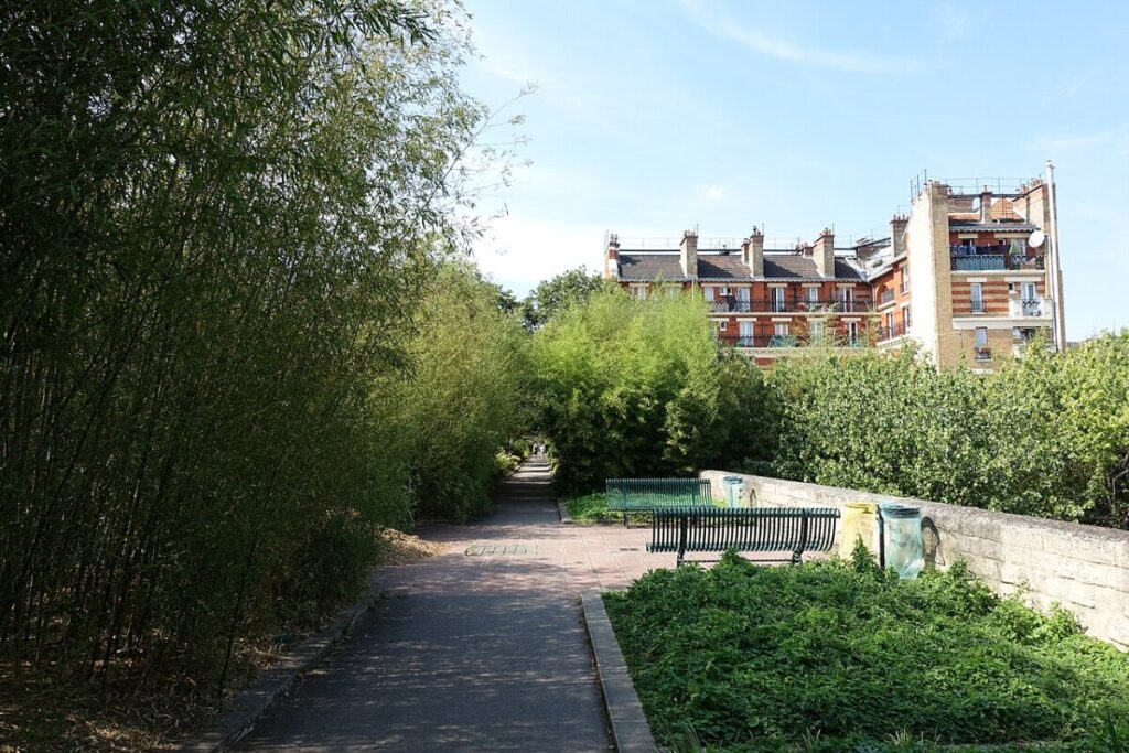Serene pathway featuring a bench, with a building visible in the background at Coulée Verte René-Dumont.
