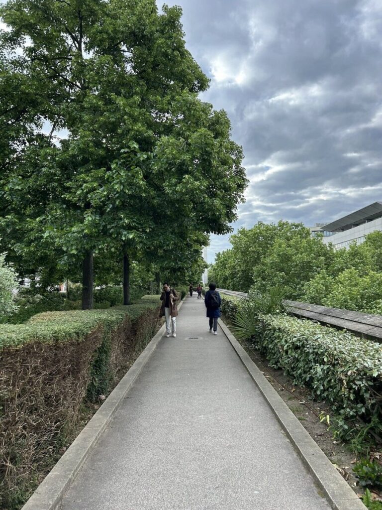 People walking along a scenic path in Coulée Verte René-Dumont Park, surrounded by greenery and trees.