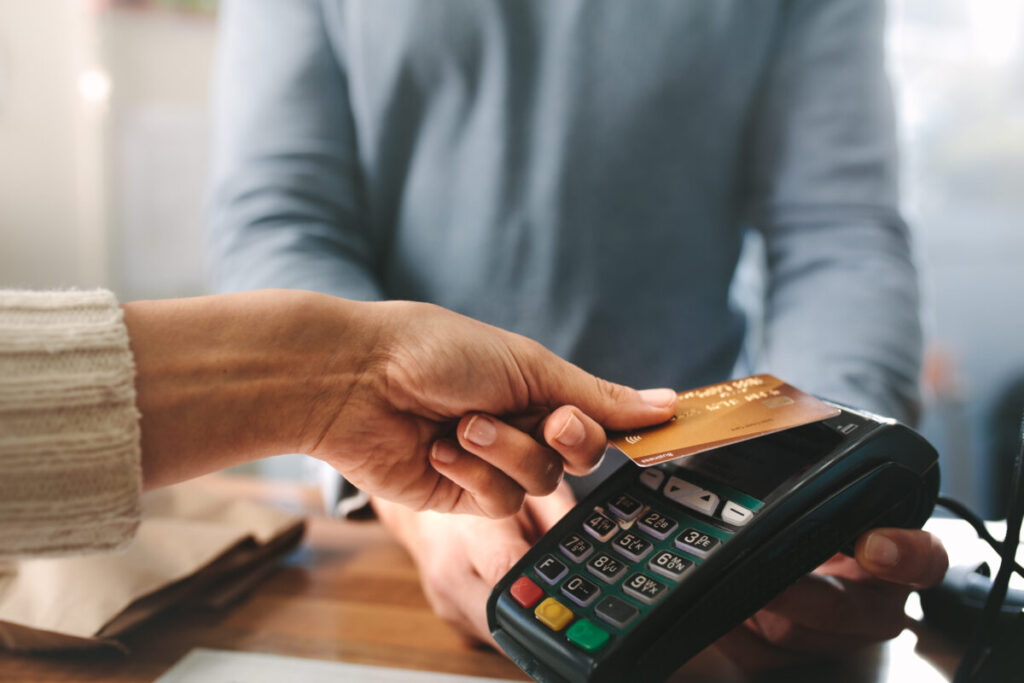 Close-up of a hand holding a credit card near a contactless payment reader.