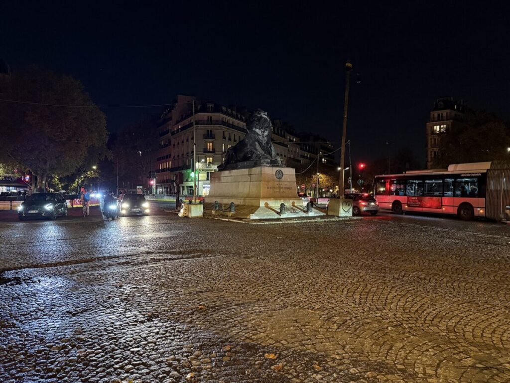 Nighttime view of Denfert-Rochereau in Paris, showcasing a street with a prominent statue of a man.