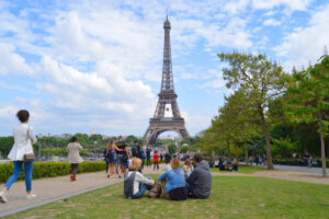 People relax on the grass in front of the Eiffel Tower, enjoying a sunny day at the Eiffel Tower Grounds in Paris.