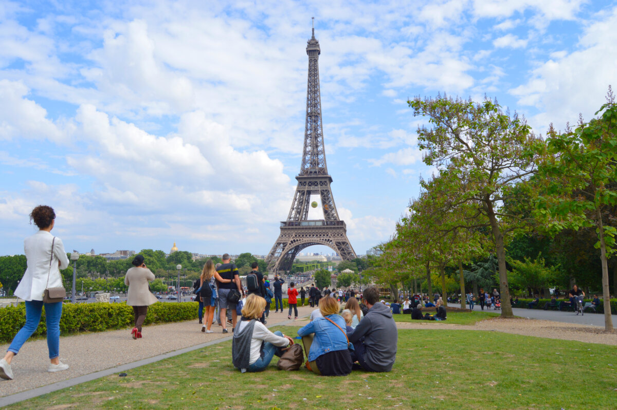 People relax on the grass in front of the Eiffel Tower, enjoying a sunny day at the Eiffel Tower Grounds in Paris.