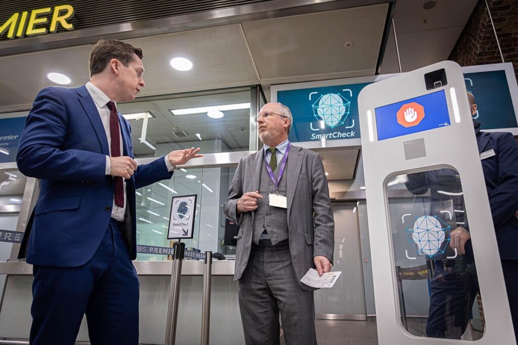 Two men in suits stand beside a machine related to the European Entry and Exit System.