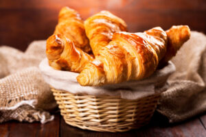 Close-up of fresh, golden croissants nestled in a woven basket, showcasing their flaky texture and inviting appearance.