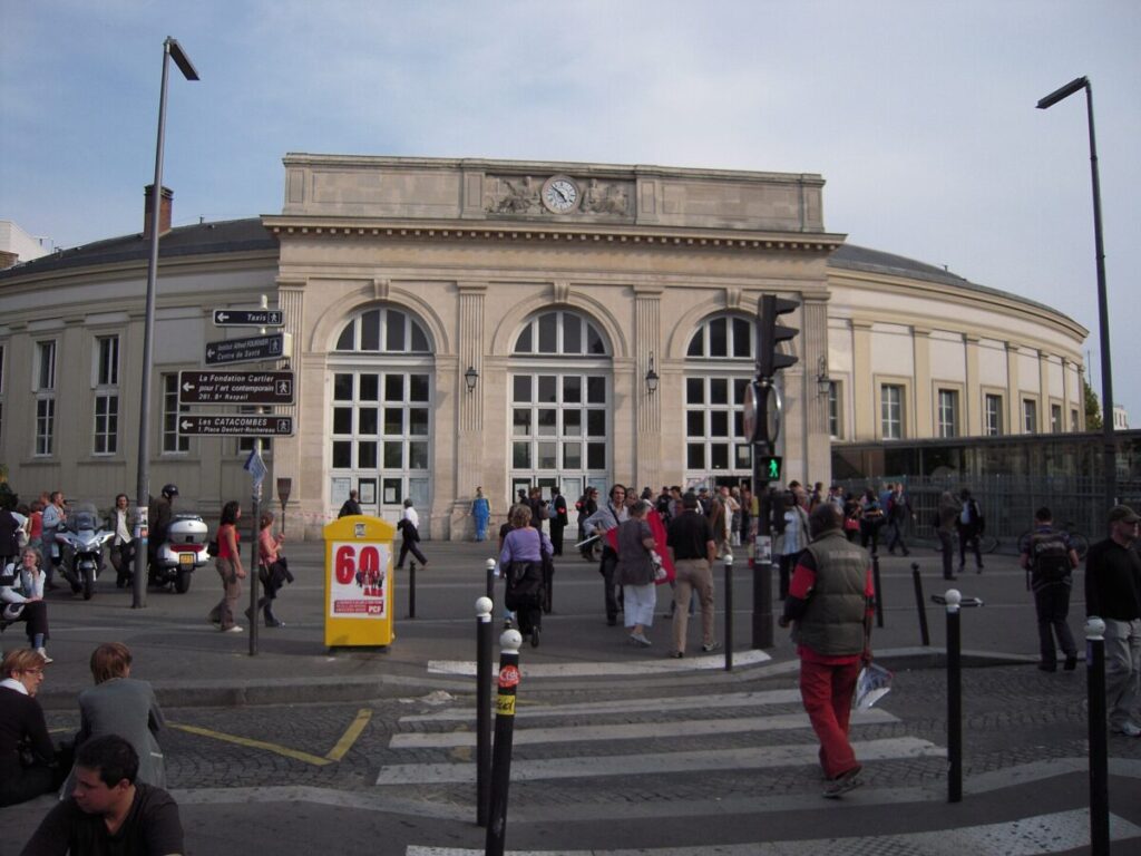 Prominent building with many windows, representing Gare Denfert Rochereau in Paris.