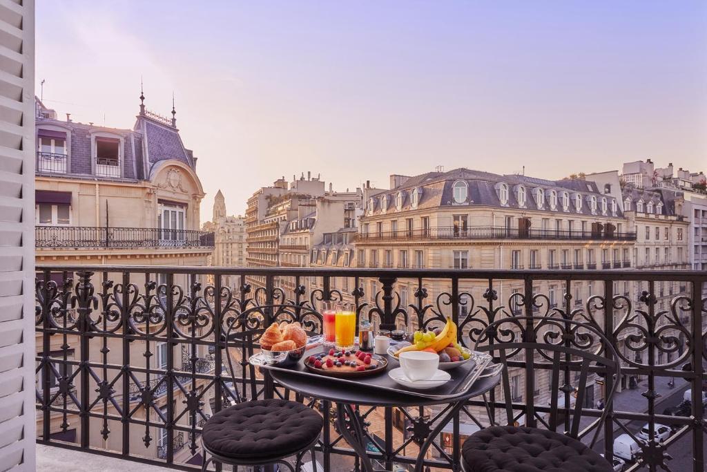 A balcony breakfast setup overlooking Parisian streets, with croissants, fruit, coffee, and juice, creating an inviting morning scene.
