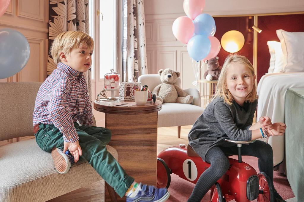 Two children enjoying a playful moment in a hotel room decorated with balloons and a teddy bear, with a sense of warmth and welcome.