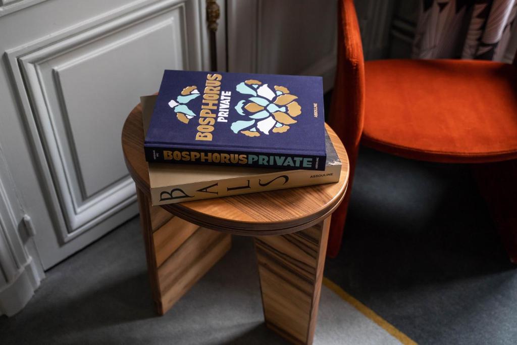 A stylish wooden side table displaying a stack of books with the top one titled "Bosphorus Private" in a chic room setting.
