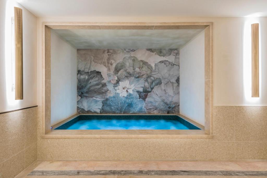 An indoor mural of oversized flowers behind a built-in tranquil blue soaking tub in a serene bathroom setting.