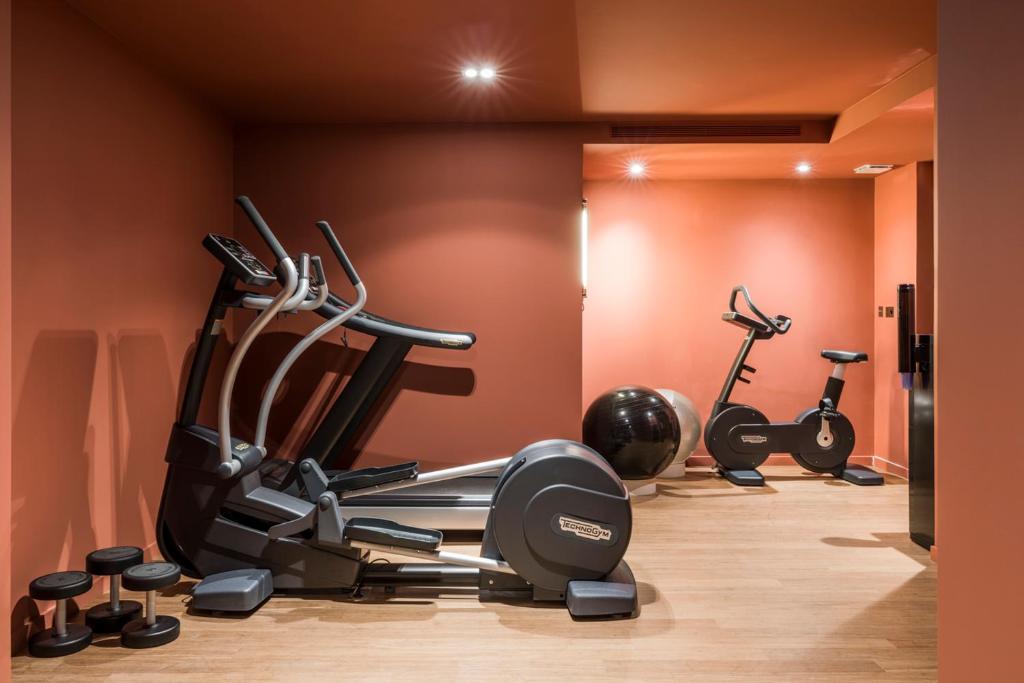 A well-equipped hotel gym with cardio machines and weights, set against a warm orange wall for a motivational workout environment.