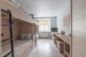 Interior of a hostel dormitory with several plain white bunk beds organized in a communal sleeping area.