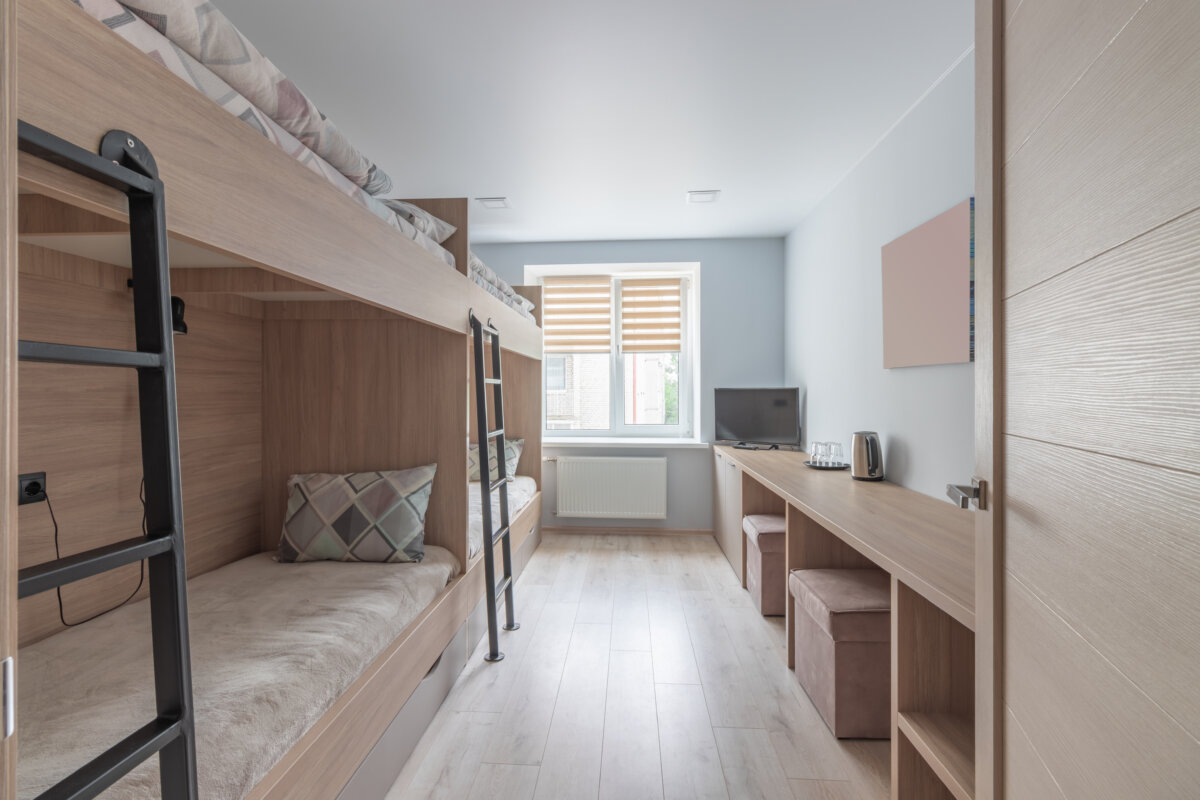 Interior of a hostel dormitory with several plain white bunk beds organized in a communal sleeping area.