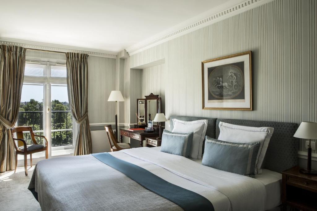 Spacious and elegantly furnished hotel room at Hôtel Brighton - Esprit de France, featuring plush bedding, classic decor, and large windows with a view of Paris.