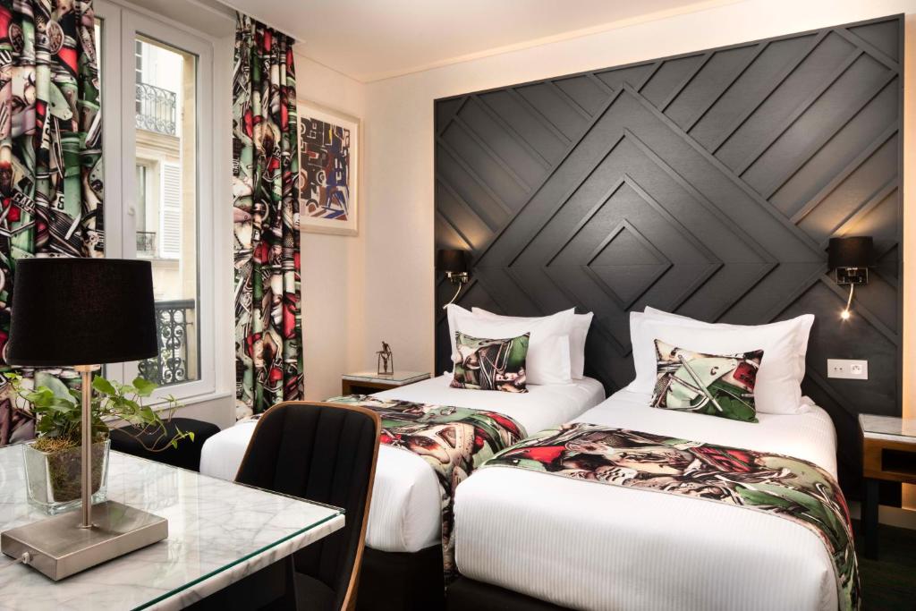 Hotel room at Hôtel des Arts Montmartre featuring two beds and a table, designed for comfort and relaxation.