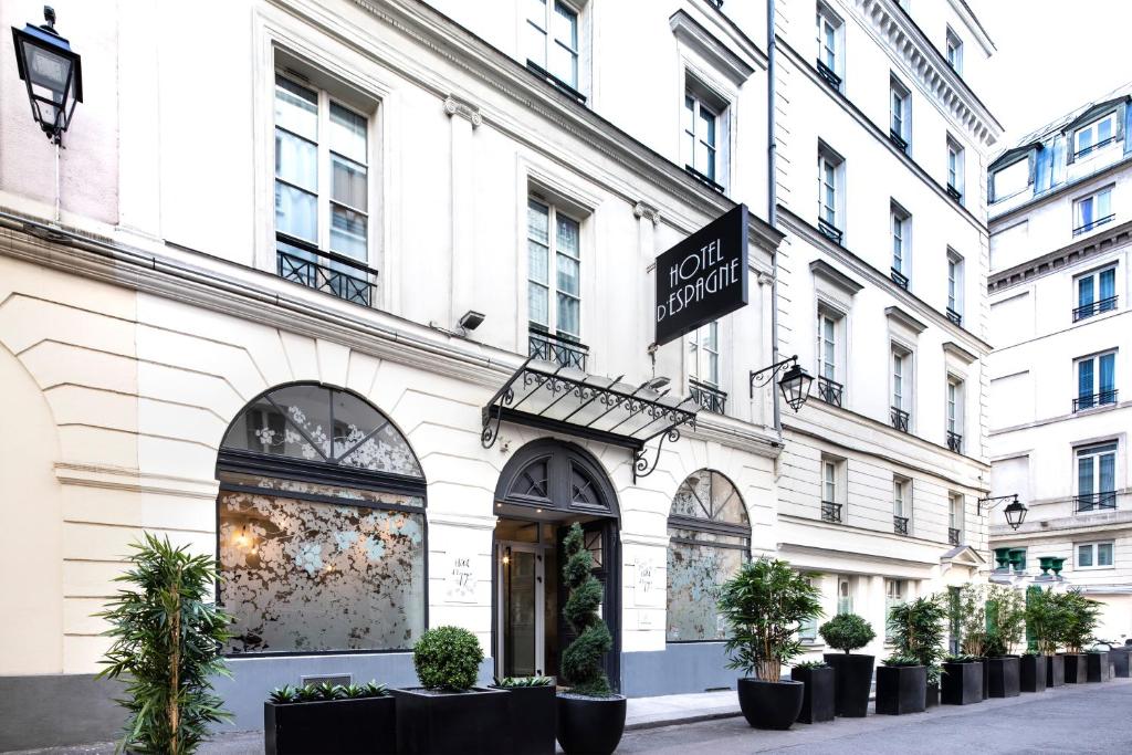 The elegant facade of Hotel d'Espagne, showcasing ornate architectural details, wrought iron balconies, and flower boxes against a backdrop of clear blue sky.